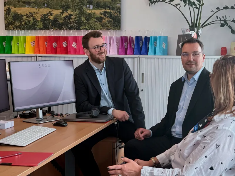 Drei Kolleg:innen der Abteilung Organisation im täglichen Austausch miteinander in einem unserer hellen Büroräume.